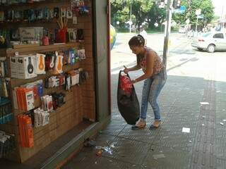 Funcionária de banca de artigos eletrônicos precisou limpar a calçada na manhã desta quarta-feira, mesmo com o retorno do serviço de coleta. (Foto:Flávia Lima)