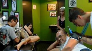 Roberto Higa começando a tatuagem e Sandra, a esposa, ao fundo, morrendo de medo. 