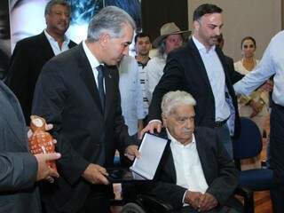 Na cadeira, Pedrossian recebe homenagem das mãos de Reinaldo, durante cerimônia na Uems (Universidade Estadual de Mato Grosso do Sul) (Foto: Marcos Ermínio/Arquivo)