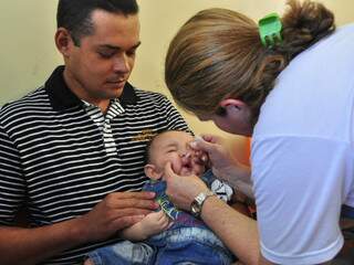 Criança recebe a gotinha da vacina contra paralisia infantil no colo do pai: proteção. (Foto: João Garrigó)