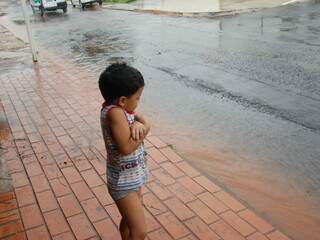 Com os pés no chão, menino observa a chuva no bairro Cabreúva.