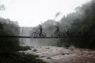 Atleta cruzam a ponte com uma cachoeira de fundo no Parque Natural Municipal Salto do Sucuriú (Foto: Paulo Francis)