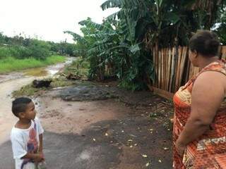 Luzinete e um dos filhos olhando rua de terra tomada pela água da chuva (Foto: Danielle Valentim)