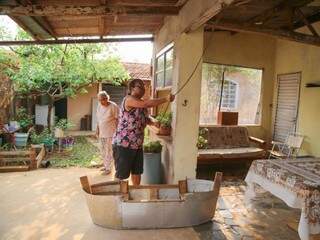 Raquel da Silva Santos pendurando o balanço na varanda, aos fundos, sua mãe Giselia da Silva (Foto: Alana Portela)