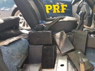 Tabletes de cocaína estavam camuflados de pretos, sob assoalho de veículo. (Foto: Divulgação/PRF) 