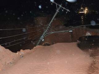 Erosão chegou ao asfalto e levou poste, que está pendurado pelos fios de alta tensão (Foto: Simão Nogueira)