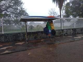 Estudantes tentando se proteger da chuva em ponto de ônibus com rua alagada pela chuva desta tarde (Foto: Geisy Garnes)