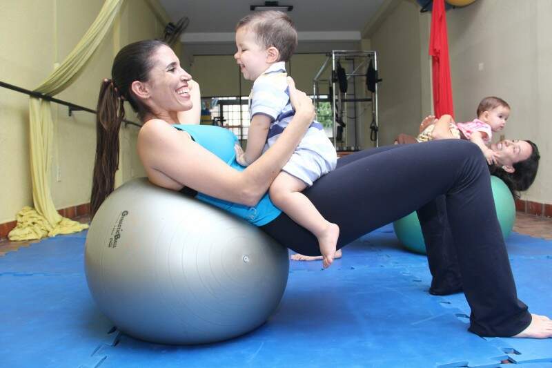 Mães fazem exercícios enquando os bebês se divertem em aula de