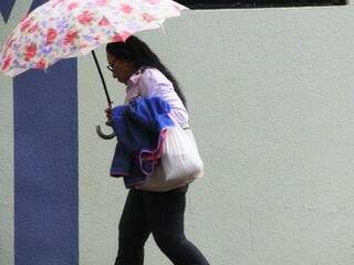 Mulher se protege da forte chuva que cai em Campo Grande nesta terça-feira (Foto: Marcos Ermínio)