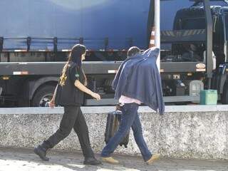 Homem preso em Campo Grande ao chegar à sede da PF escondendo o rosto e com mala na mão (Foto: Saul Schramm)