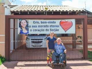 Cristina Dantas e o marido Paulo Sérgio Moreno de Jesus na frente do portão da casa onde o esposo colocou a faixa de declaração (Foto: Alana Portela)