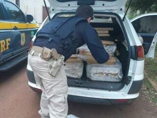 Agente da PRF retirando os tabletes de droga do porta-malas. (Foto: Divulgação/PRF)  