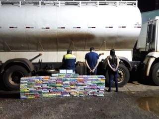 Suspeitos ao lado da pilha de tabletes de droga que estavam escondidos em fundo falso de caminhão. (Foto Divulgação/Polícia Militar) 