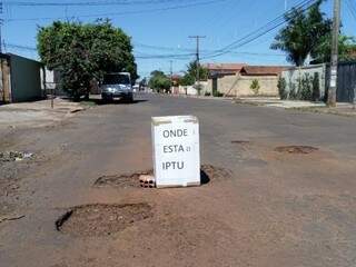 Placa com a mensagem &quot;Onde está o IPTU&quot; sinalizando um buraco na Av Aeroporto, bairro Sto Amaro em Campo Grande (Foto: Direto das ruas) 