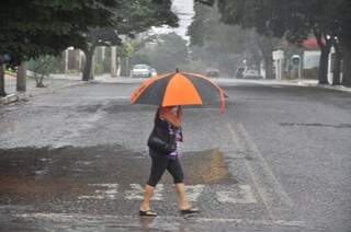 Mulher com guarda chuva atravessando rua esta tarde na Capital (Foto: João Garrigó)