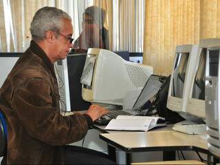 Jorge Luis da Silva de Jesus, de 56 anos. Ao lado de um dos computadores disponibilizados ao público, ele liga o notebook próprio.