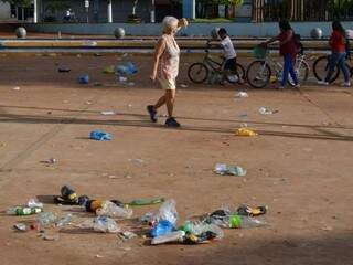 Moradores passam por lixo deixado na praça por foliões de Carnaval improvisado (Foto: Vinicios Araújo/Dourados News)