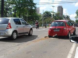 Motorista do carro vermelho tenta desviar, mas acaba caindo em buraco no cruzamento da Padre João Crippa com Afonso Pena. (Foto: Alan Diógenes)