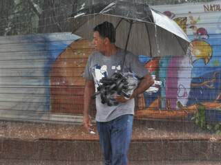 Aproveitando para ganhar dinheiro, vendedor tem nos braços a proteção contra a chuva. (Foto: Simão Nogueira)