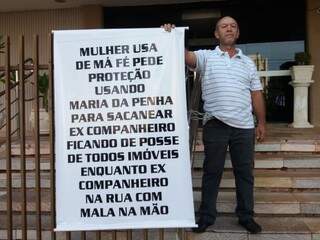 Nesol, acorrentado à escada, segura o cartaz com dizeres contra ex-companheira. (Foto: Osvaldo Duarte/Dourados News).