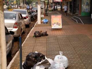 Sacos de lixo acumulados na Avenida Marcelino Pires, no centro de Dourados (Foto: Adilson Domingos)