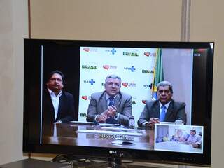 O secretário Leandro Mazina, ministro da saúde Alexandre Padilha e governador André Puccinelli (PMDB) anunciaram recursos em videoconferência. (Foto: Pedro Peralta)