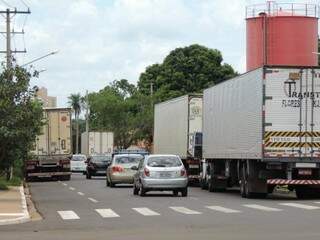 Na via mão única, caminhões estacionados dos dois lados da rua atrapalham o trânsito.