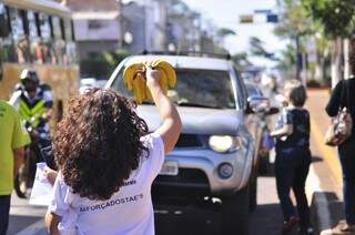 Servidora da UFGD distribui banana em semáforo da Avenida Marcelino Pires, nesta quinta (Foto: Eliel Oliveira)