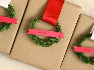 Embalagem de papel pardo, com fita e um pedaço de galho de árvore de Natal em formato de circulo. Para fechar, um pedaço de papel Color7, para o nome do destinatário.