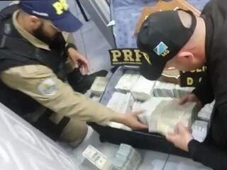 Policiais rodoviários federais fazem contagem de dólares encontrados com casal. (Foto: Divulgação/DOF)