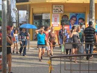 Pessoas andando por rua do Centro de Campo Grande e tentando tapar o sol até com a mão (Foto: Marina Pacheco)