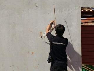 Perito da Polícia Civil analisa pegada no muro da casa onde servidor foi encontrado morto (Foto: Adilson Domingos)