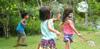 Crianças brincam com raquete de bolhas de sabão.
