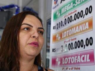 Dona de lotérica em frente ao cartaz que aponta para o prêmio de R$ 280 milhões da Mega da Virada (Foto: Kisie Ainõa) 