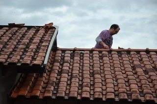 Na tentativa de amenizar o estrago, morador se arrisca e sobe no telhado para arrumar telhas (Foto: Cleber Gellio)