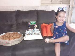 Isa sentada no sofá ao lado do bolo, pastéis e dos presentes (Foto: Arquivo pessoal)