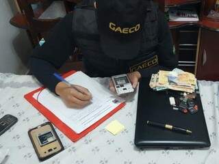 Dinheiro e celulares, apreendidos durante operação, sendo contabilizados por agente do Gaeco. (Foto: Divulgação/ Gaeco)