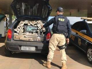 Policial contando a quantidade de tabletes de droga encontrados no porta-malas do veículo. (Foto: Divulgação/PRF) 