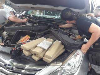 Policiais fazendo a retirada da droga do compartimento oculto do carro. (Foto: AgoraMS) 