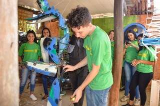 O estudante amassando lata com o auxílio de uma máquina (Foto: Alana Portela)