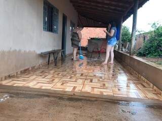 Sirlene Dias e a filha limpam varanda tomada pela enxurrada. Na parede, é possível ver a altura que água atingiu durante a chuva (Foto: Liniker Ribeiro)