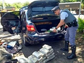 Policial fazendo a contagem dos tabletes de droga encontrados no porta-malas de veículo (Foto: Panorama Notícias) 