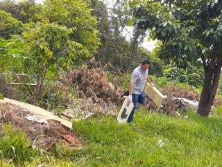 Agente de saúde recolhe objetos em terreno sujo de Campo Grande (Foto: PMCG/Divulgação)