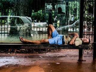 Sem teto, morador de rua deita no banco do terminal de ônibus que está na Praça Ary Coelho, em Campo Grande (Foto: Marcos Maluf)