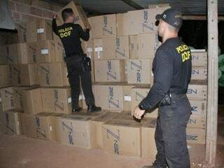 Agentes do DOF empilham caixas de cigarro encontradas em depósito de contrabandistas, em Mundo Novo (Foto: Divulgação/DOF)