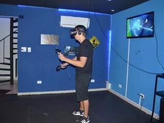 O jogador precisa colocar o óculos e segurar dois controles para poder interagir no jogo de realidade virtual. (Foto: Alana Portela)