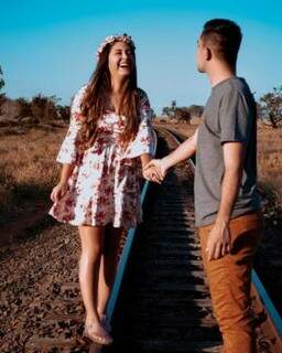 Casal no trilho do trem, sob o céu azul campo-grandense. (Foto: Mari Tavora)