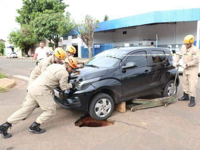Asfalto cede e motorista de aplicativo tem carro preso em buraco