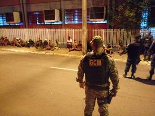 Sentados na calçada, moradores de rua são observados por guardas civis municipais. (Foto: Divulgação)