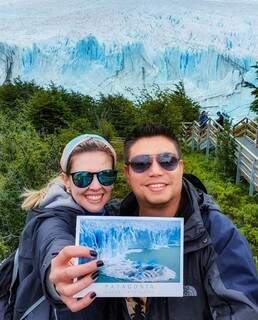 Daniela Barros ao lado de Thiago Kussano, segurando um cartão postal na Geleira Perito Moreno, na Argentina. (Foto: Arquivo pessoal)